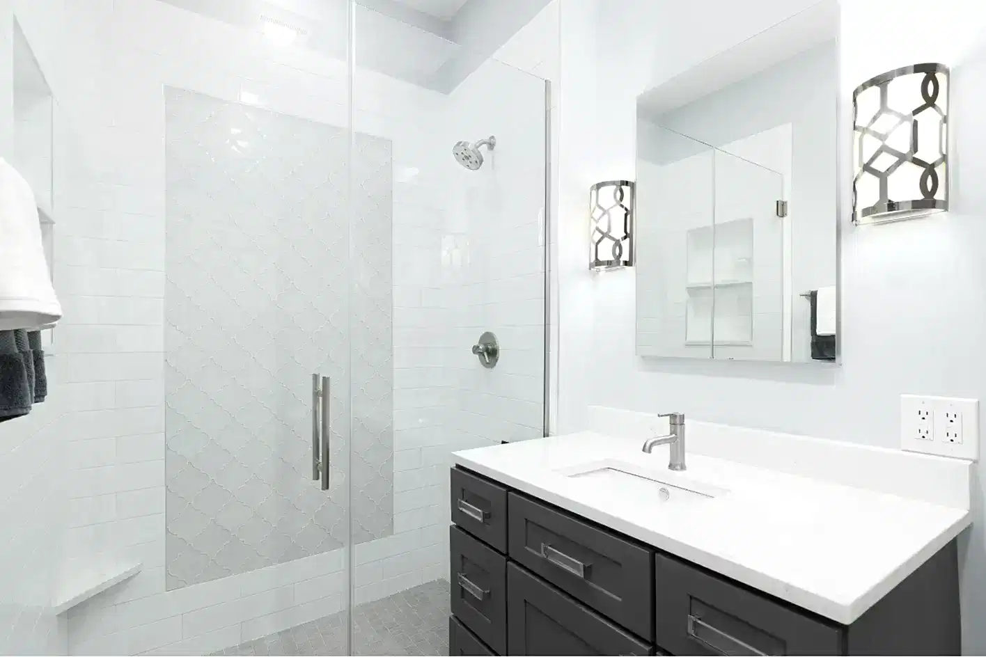 Beyaz metro fayanslı duş ve koyu gri banyo dolabı.