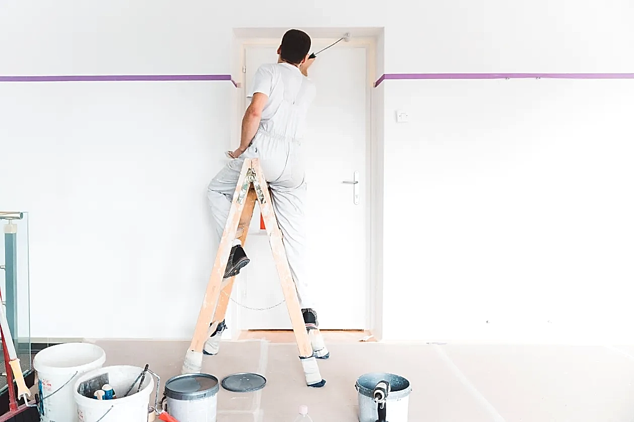 Salon duvarlarını rulo ile boyayan tulumlu profesyonel iç cephe boya ustası