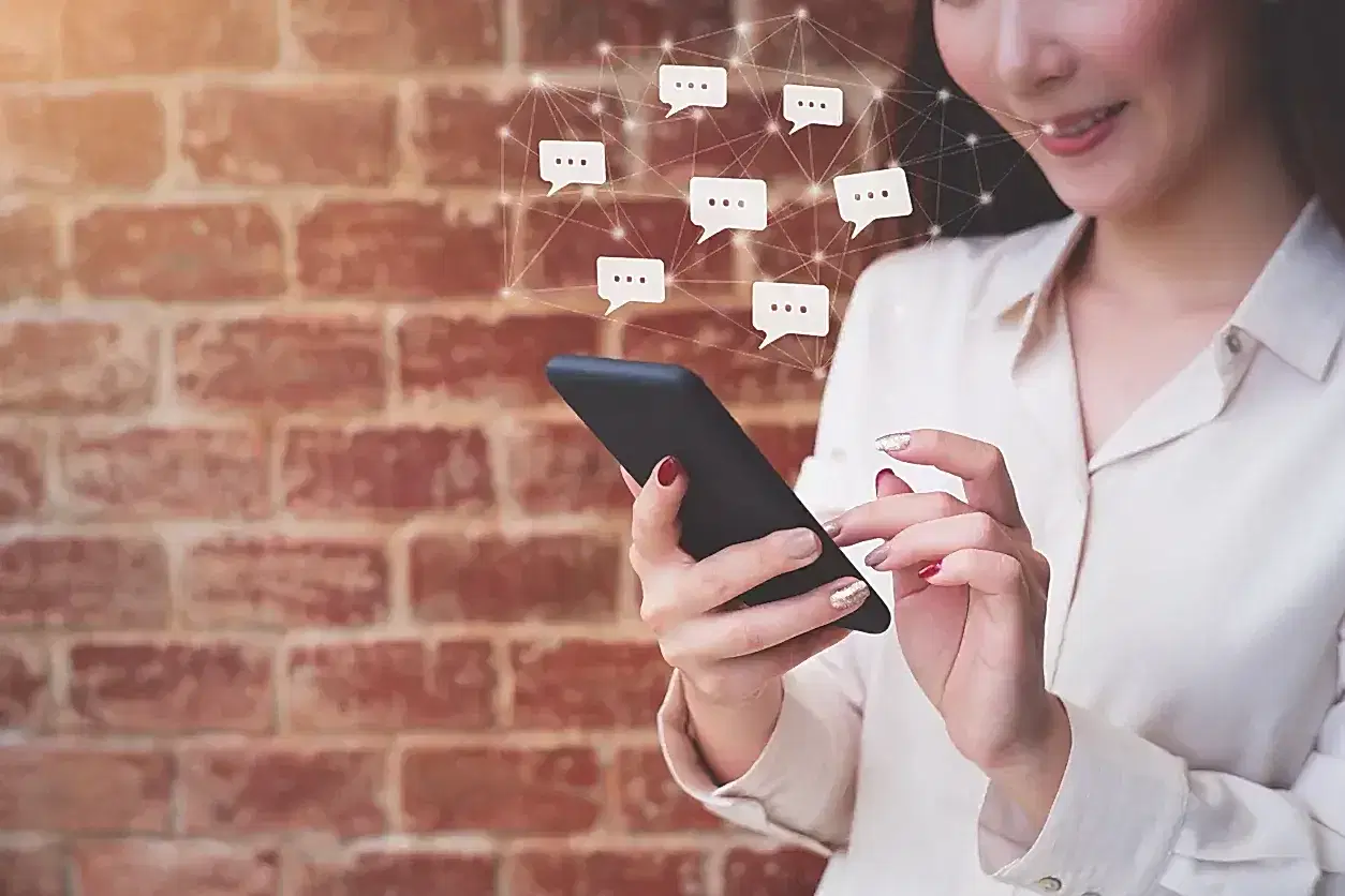 Tuğla duvar önünde akıllı telefon kullanan kadın ve dijital iletişim ikonları.